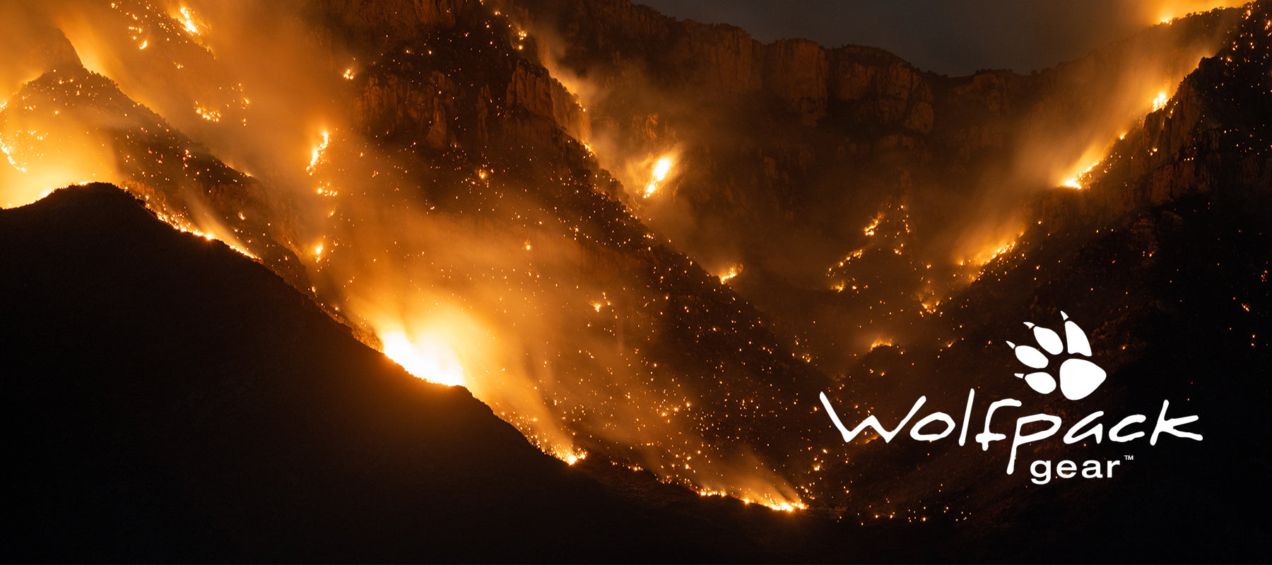 Wolfpack Gear™ - image of a wildland fire with a valley of forest on fire at night